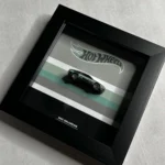 پوستر ۲۰×۲۰ سانتی‌متری با تصویر ماشین هات ویلز مدل DMC DeLorean مشکی، روی پس‌زمینه‌ای با نوارهای رنگی و لوگوی هات ویلز، در قابی مشکی.