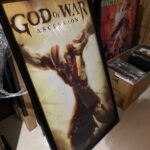 پوستری با ابعاد 60x40 یا 70x40 سانتی‌متر از جلد بازی "God of War: Ascension" که کریتوس را در مرکز با بازوهای باز و زنجیرهایش در حال فریاد زدن قدرت نشان می‌دهد. پس‌زمینه با نورهای طلایی و مایل به قهوه‌ای روشن است و عنوان "GOD OF WAR ASCENSION" در بالای پوستر دیده می‌شود.